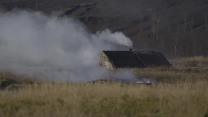 Steam rises from a geothermal hot spring and a rustic hut's chimney in a vast, grassy landscape