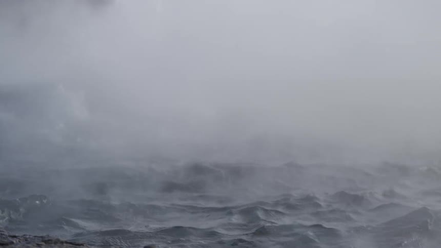 Thick gray steam billows from the surface of a churning geothermal hot spring