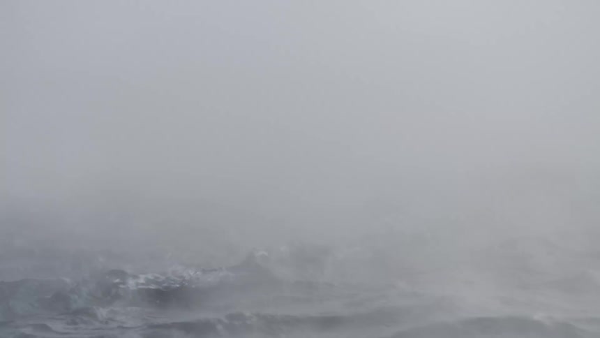 Mysterious mist and fog swirl over the dark, turbulent waves of the ocean in slow motion
