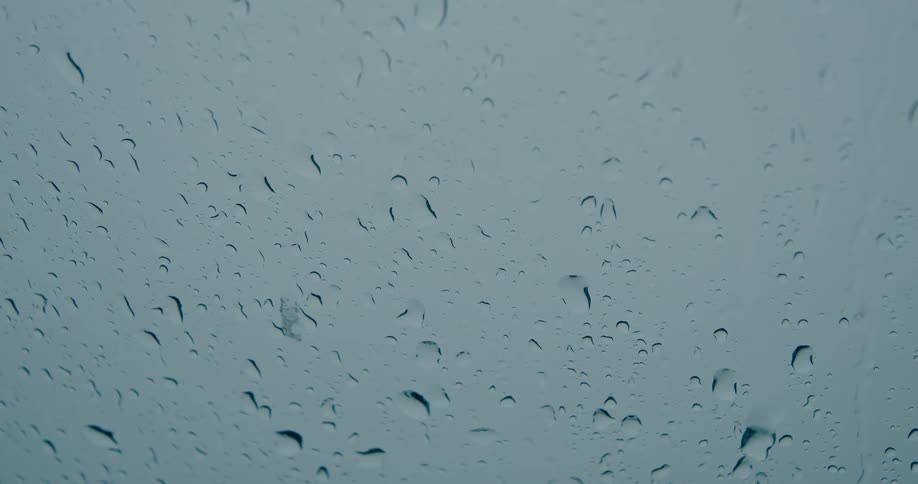 Close-up of raindrops trickling down a window pane on a cloudy day