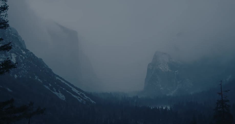 A slow zoom out of a moody, foggy, snowy mountain valley during a winter storm