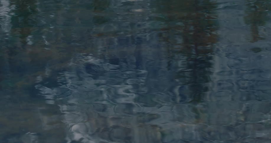 Top-down view of a dark, calm water surface with gentle ripples creating abstract reflections