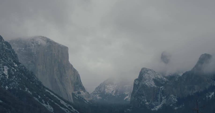 A dramatic tilt-down shot reveals the snow-covered and fog-shrouded Yosemite Valley from the Tunnel View overlook in winter