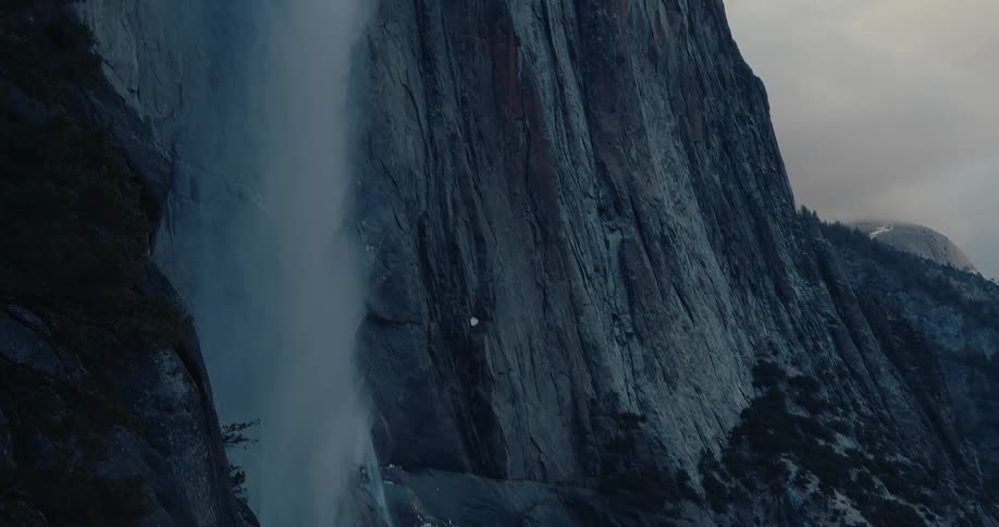 Majestic waterfall tumbles down a sheer granite cliff in the moody, snowy Yosemite National Park