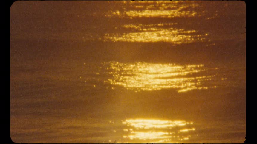 The warm, golden reflection of the sun dances on the gentle ripples of the water in a nostalgic, vintage clip