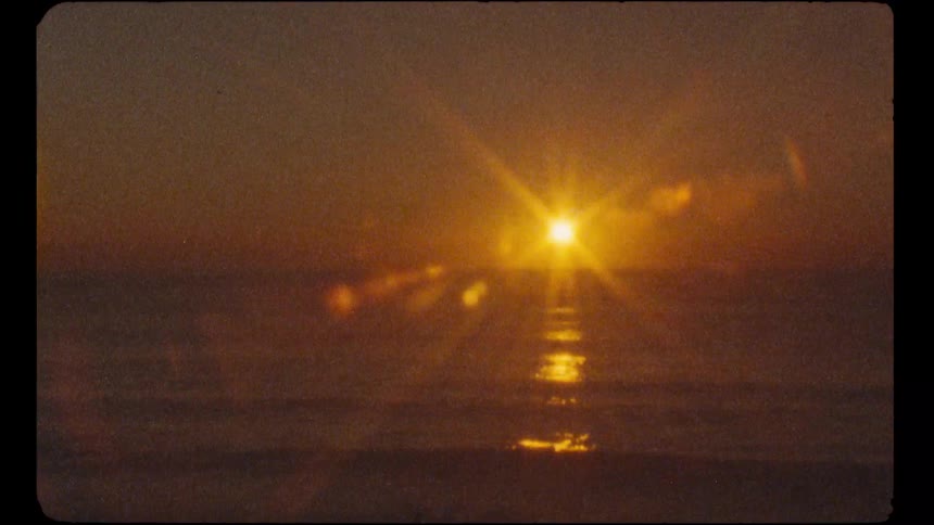 A nostalgic Super 8mm film captures the warm, golden sun setting over the ocean with a beautiful lens flare