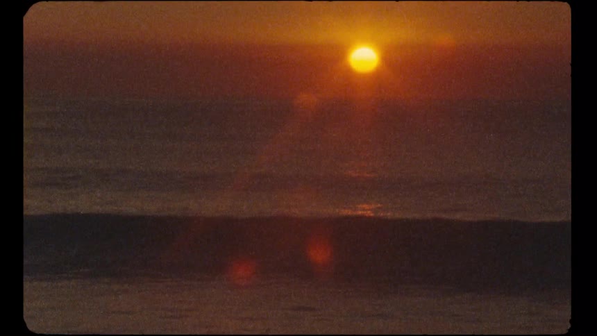 A nostalgic, grainy Super 8 film captures a beautiful golden sun setting over the calm ocean waves