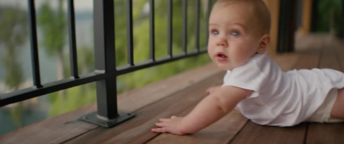 An adorable and curious baby boy with blue eyes does tummy time on a wooden deck overlooking a lake