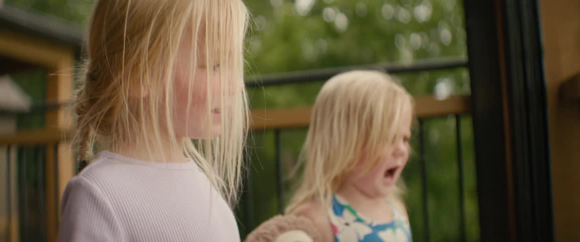 Two young blonde sisters express their emotions on a cabin porch