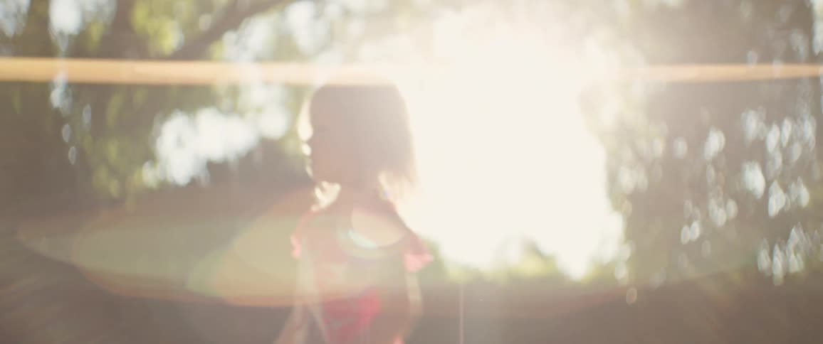 Little girl plays outdoors in warm golden sunlight while swinging a teddy bear in the backyard
