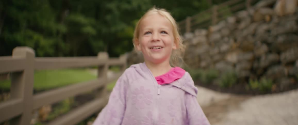 A happy little girl with blonde hair runs towards the camera with a big joyful smile on her face