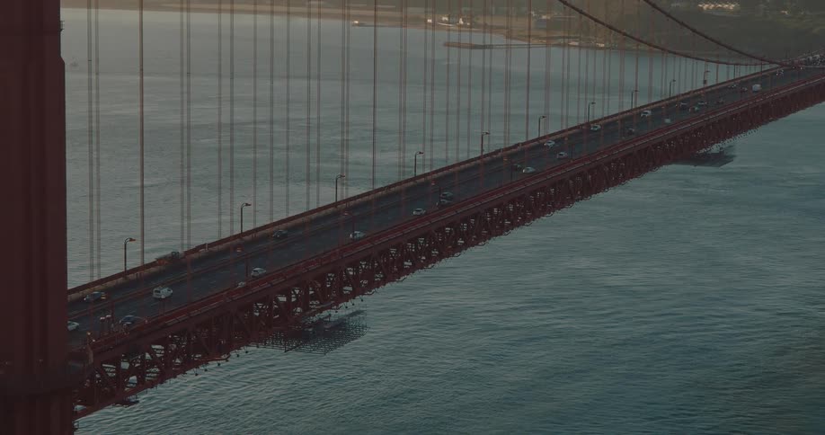 A high-angle static shot shows cars driving across the iconic Golden Gate Bridge at dusk