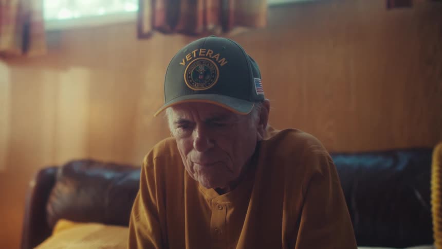 A tilt-up reveals an emotional elderly veteran sitting alone at home watching a video on his tablet
