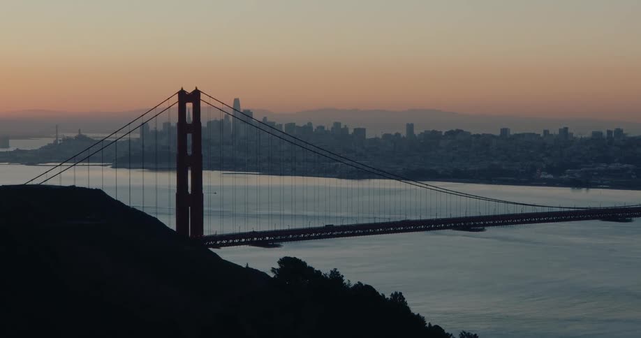 Early morning light illuminates the sky over the Golden Gate Bridge with the San Francisco skyline in the distance