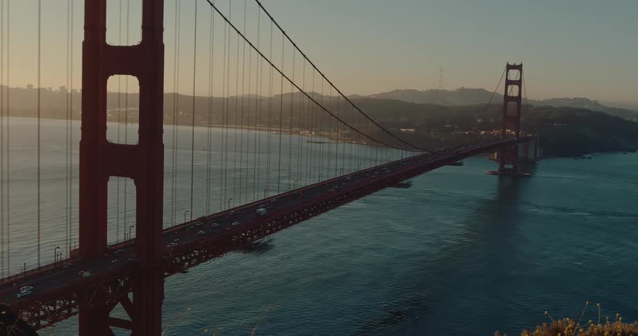 A majestic panning shot captures traffic flowing across the iconic Golden Gate Bridge during a golden sunset