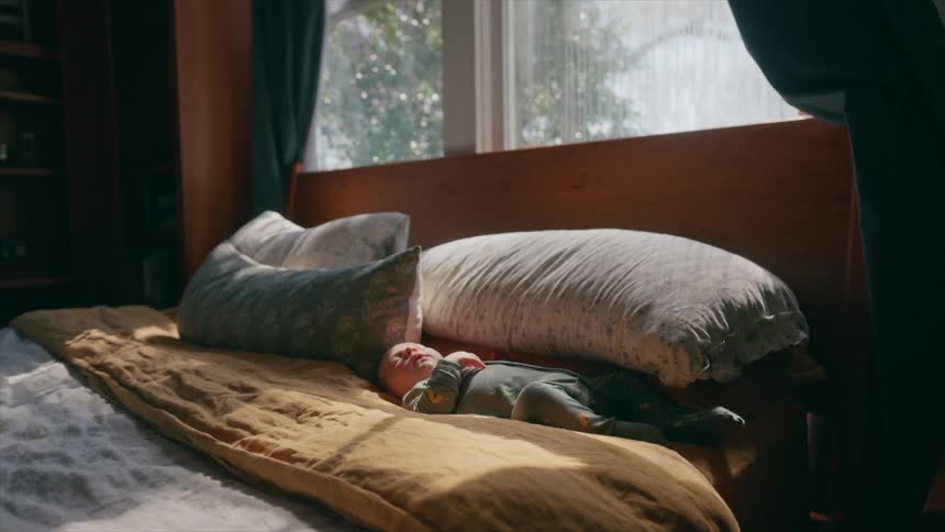 A newborn baby rests peacefully on a bed bathed in warm morning sunlight streaming through a window