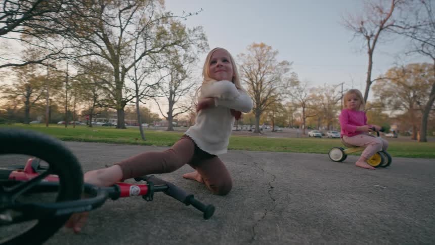 A little girl falls off her balance bike then gets up with a proud smile, ready to try again