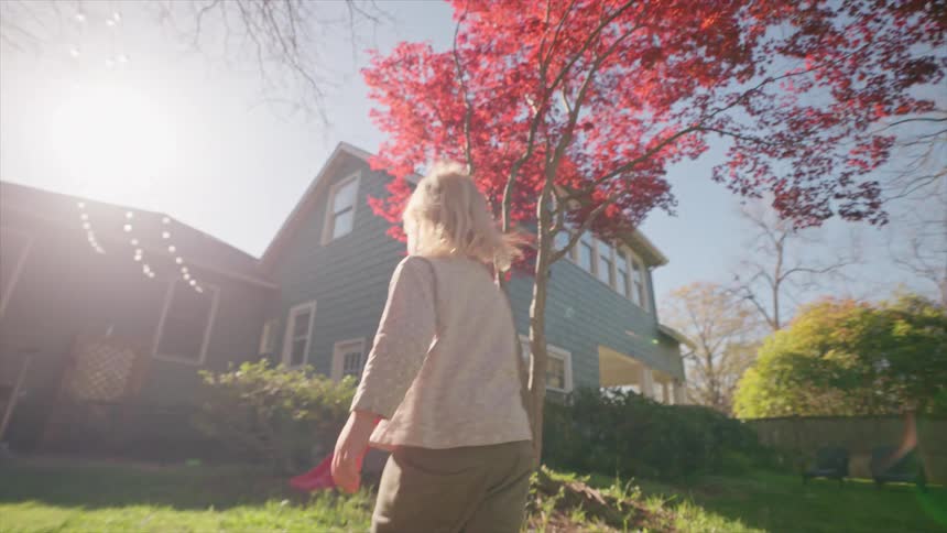 A young barefoot child walks slowly across a sunny backyard in a beautiful slow-motion tracking shot