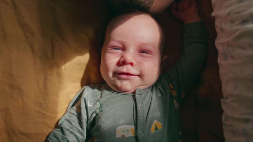 A close-up top-down view of a sweet newborn baby with blue eyes smiling happily as a sunbeam shines on their face