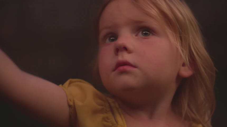 A toddler girl in a yellow dress looks up with wonder and amazement, captivated by something magical off-screen