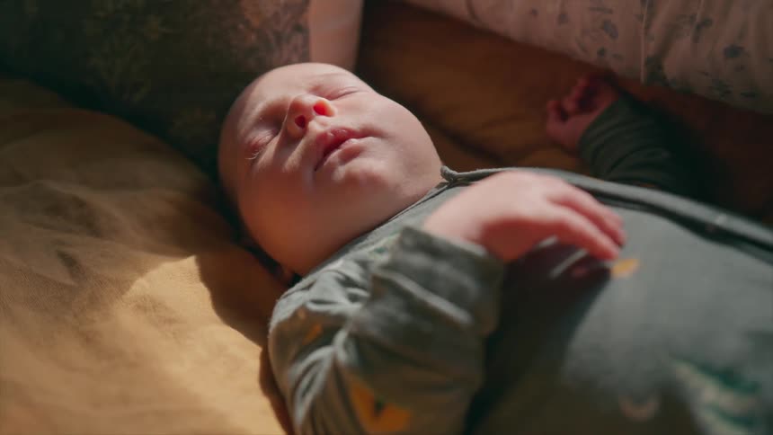 A newborn baby sleeps soundly in a crib with a warm morning sunbeam on its face
