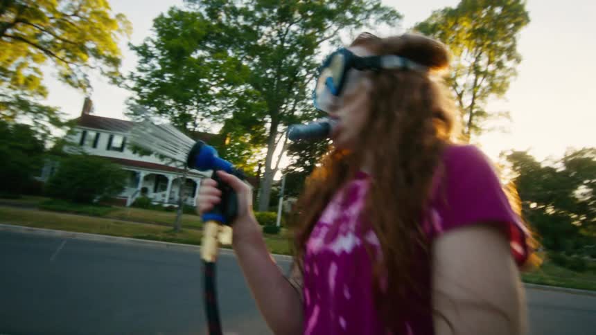 Kids wearing snorkel masks have a playful water fight with a garden hose in a suburban neighborhood at sunset