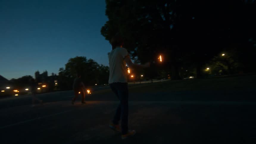 Three young friends run and dance with bright sparklers on a warm summer evening