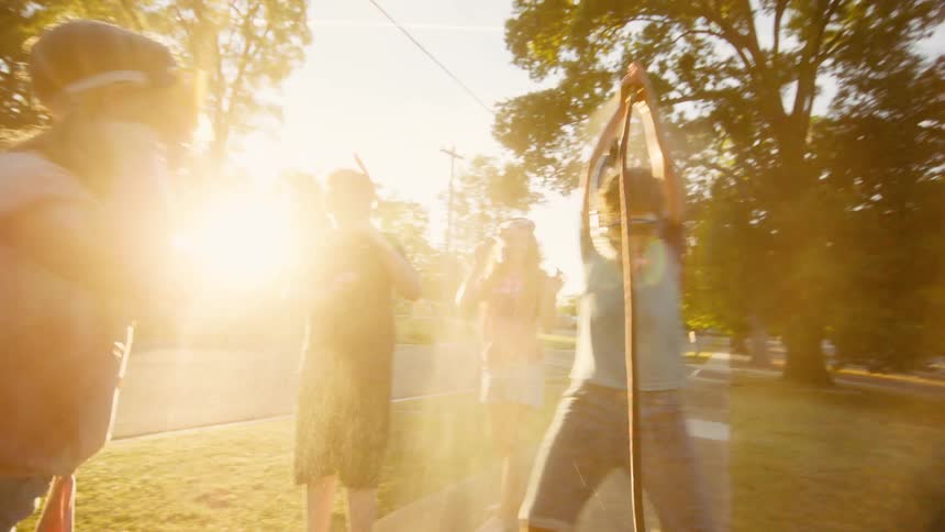 A group of children wearing snorkel masks playfully fight over a garden hose, spraying water in the golden evening sunlight