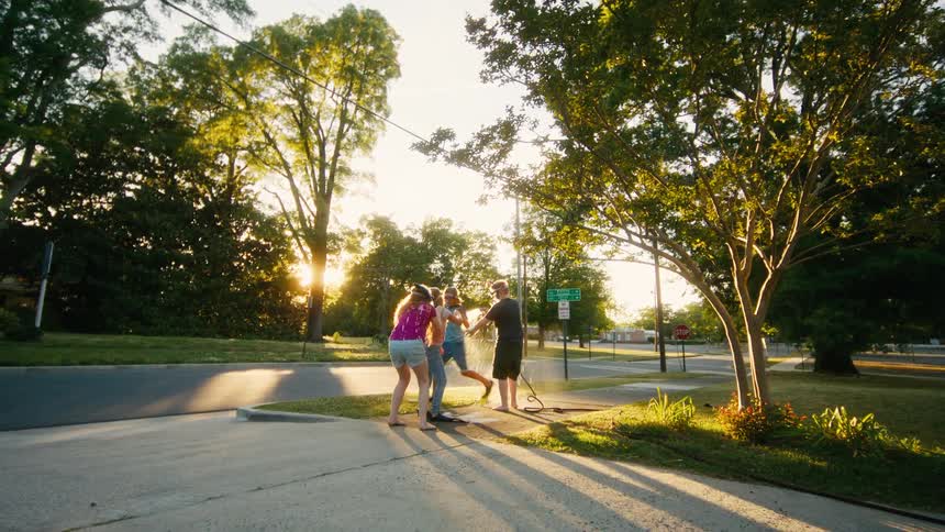 Playful friends in snorkeling gear have a slow-motion water fight with a garden hose in their driveway during a beautiful golden hour sunset
