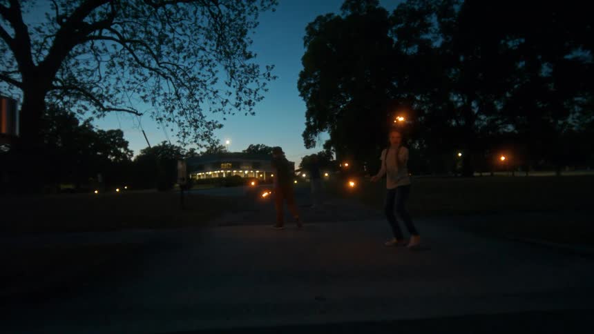 Three young friends playfully run and dance with lit sparklers in a park at twilight