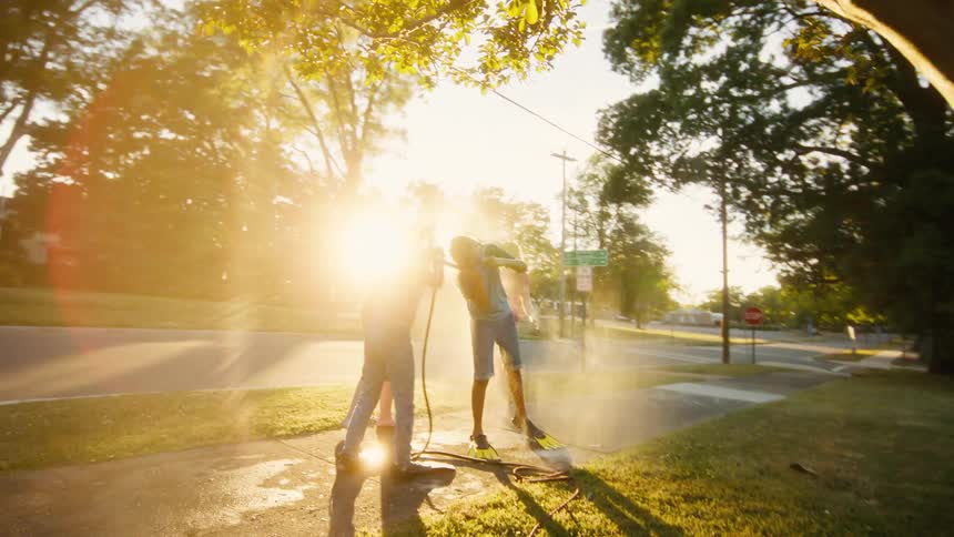 Carefree kids laugh and play with a garden hose in the golden hour sunlight on a warm summer day