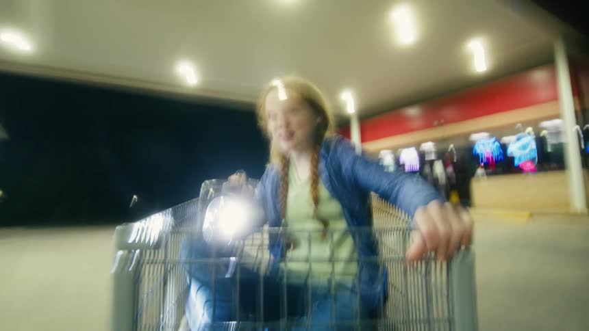 A group of kids on a nighttime adventure ride in a shopping cart with flashlights at a gas station