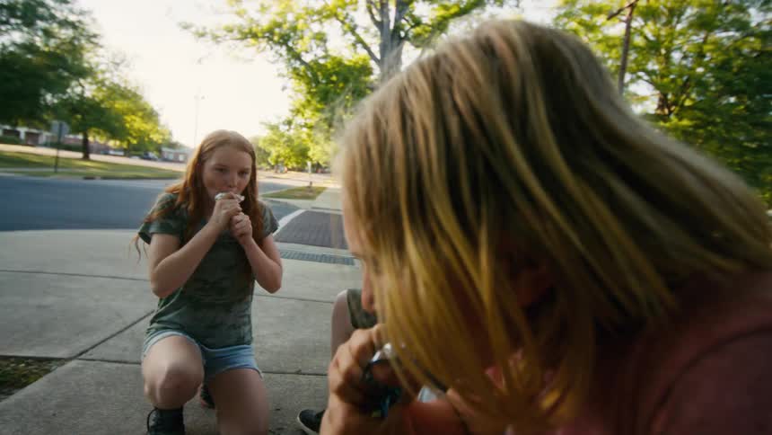 Three childhood friends share a laugh and a juice pouch break on a sunny suburban sidewalk