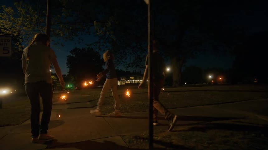 A group of children joyfully walk down a street at night, holding and playing with bright sparklers
