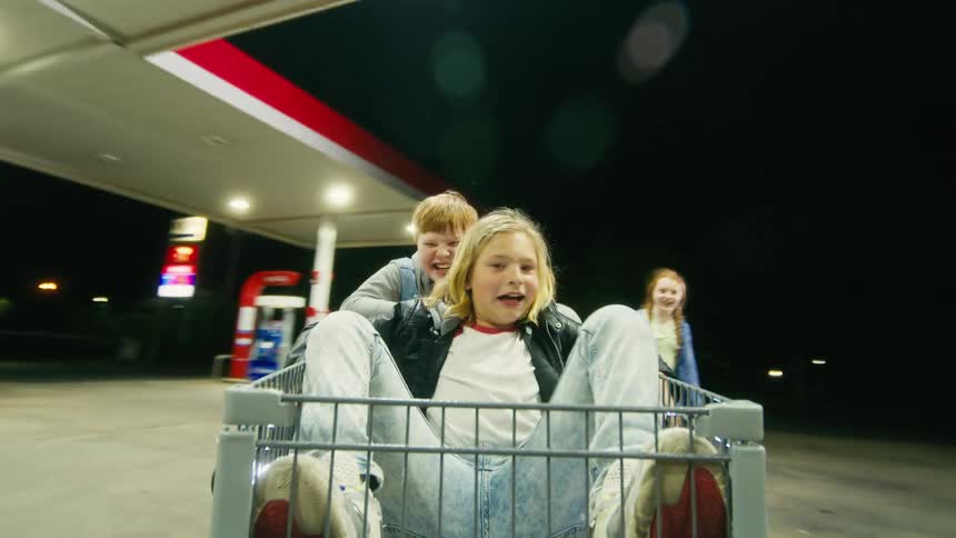 Kids on an adventurous shopping cart ride with flashlights through a gas station at night