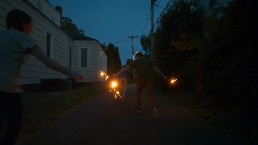 Joyful children celebrate a summer evening by running down a neighborhood alley with glowing sparklers