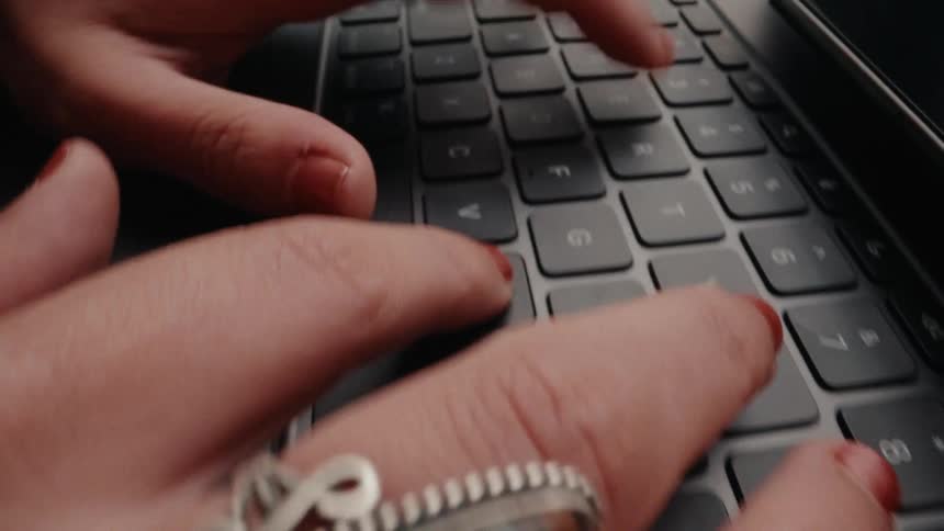 Extreme close-up of a person's hands with red nail polish and stylish rings typing quickly on a laptop keyboard