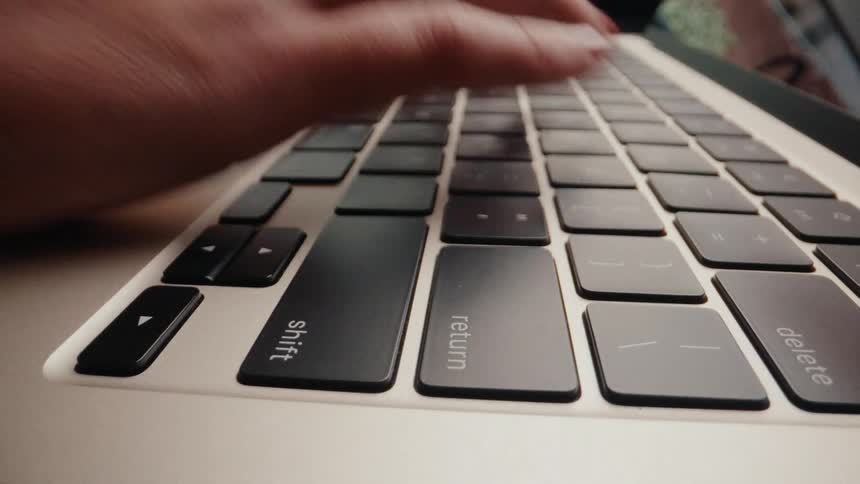 An extreme close-up shot reveals a woman's hands with red nail polish typing quickly on a laptop keyboard