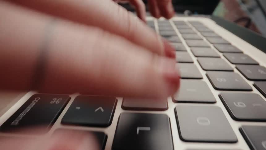 A super close-up, slow-motion shot of a woman's hands with red nail polish typing on a laptop keyboard