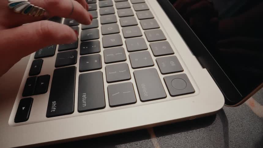 Close-up of stylish hands with rings and red nail polish typing on a modern laptop keyboard and hitting the return key