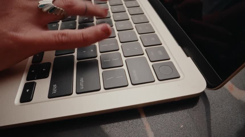 A fast-paced, close-up view of hands with red nails and rings typing on a modern laptop keyboard