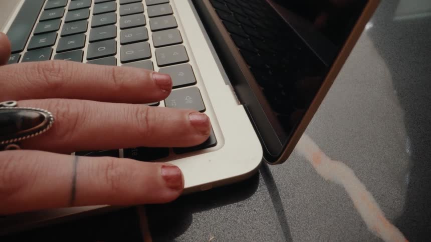 Close up of a female hand with red nail polish typing on a modern laptop keyboard
