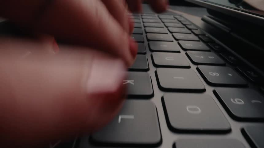 A dramatic close-up dolly shot of a woman's hands with red nails typing on a sleek black keyboard