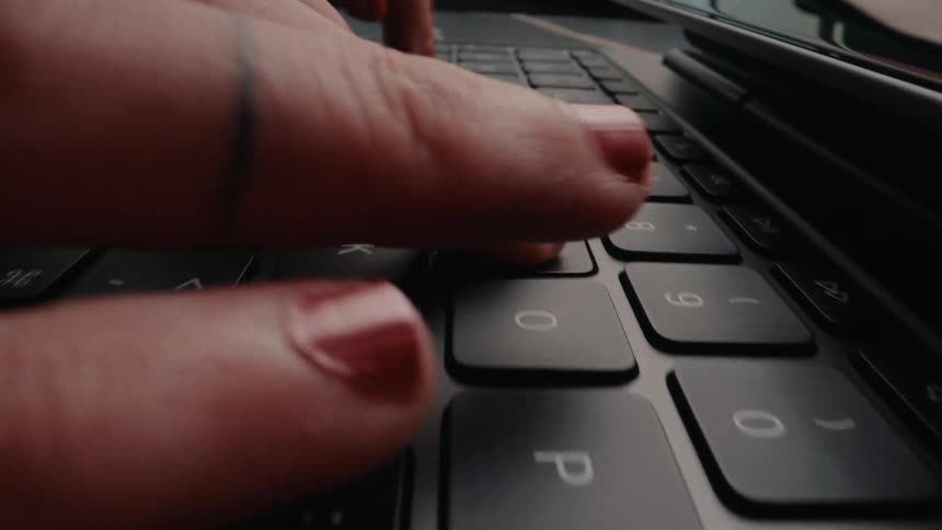 An extreme close-up shot of a woman's fingers typing on a dark computer keyboard