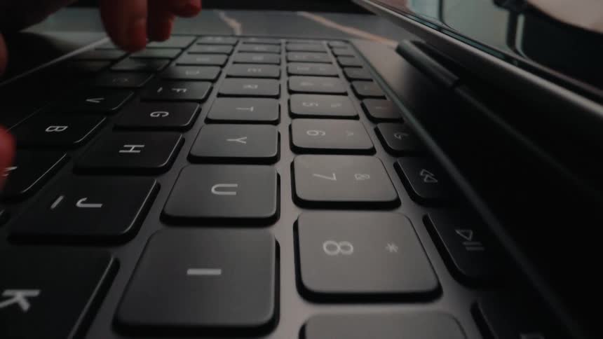 A close-up, low-angle dolly shot captures fingers with red nail polish rapidly typing on a black laptop keyboard