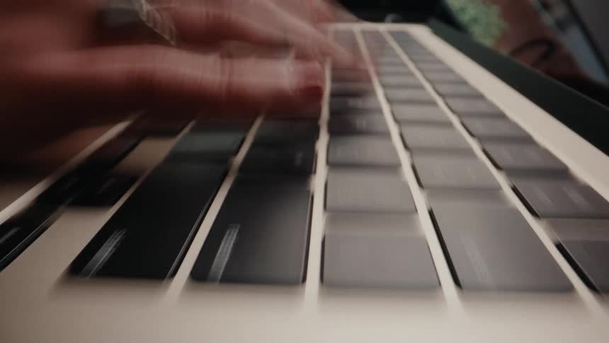 Extreme close-up shot shows a person's fingers rapidly typing on a laptop keyboard in a blur of motion
