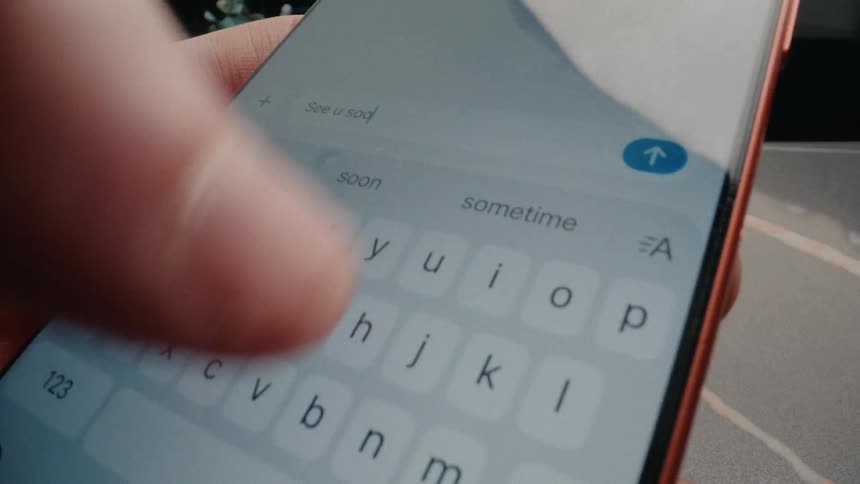 Extreme close-up of a finger typing 'See u soon!' on a smartphone's touch screen keyboard and sending the message
