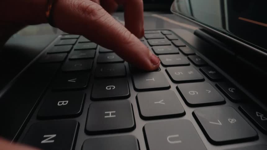 A dramatic close-up shot reveals a person's hands typing on a modern tablet keyboard as the camera slowly pulls back