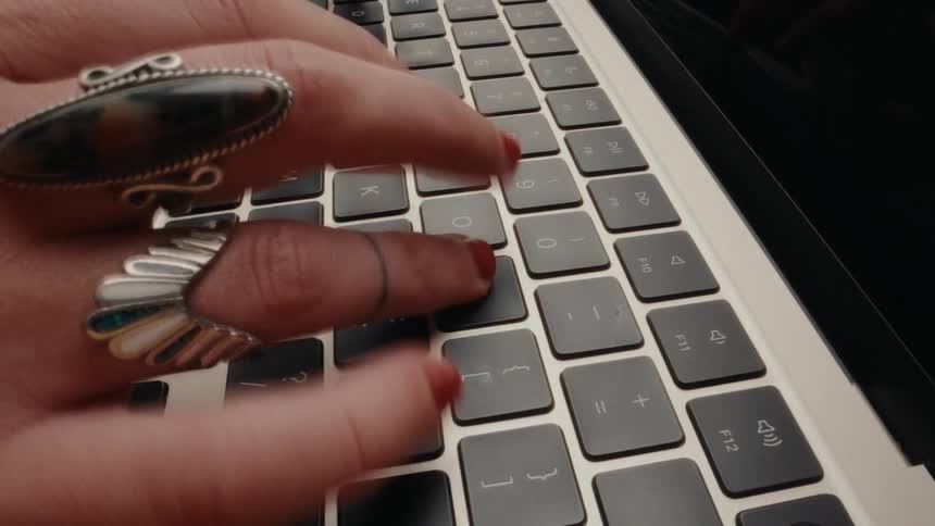 Close-up, high-speed effect shot of female hands with red nail polish and rings typing rapidly on a computer keyboard