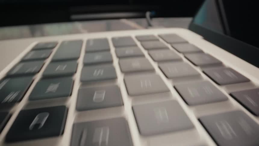 A smooth, low-angle dolly shot slides across the keys of a modern laptop keyboard on a desk